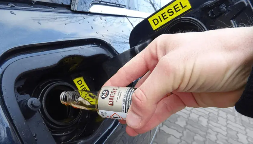 Dłoń wlewa dodatek do benzyny do baku samochodu z napisem DIESEL.