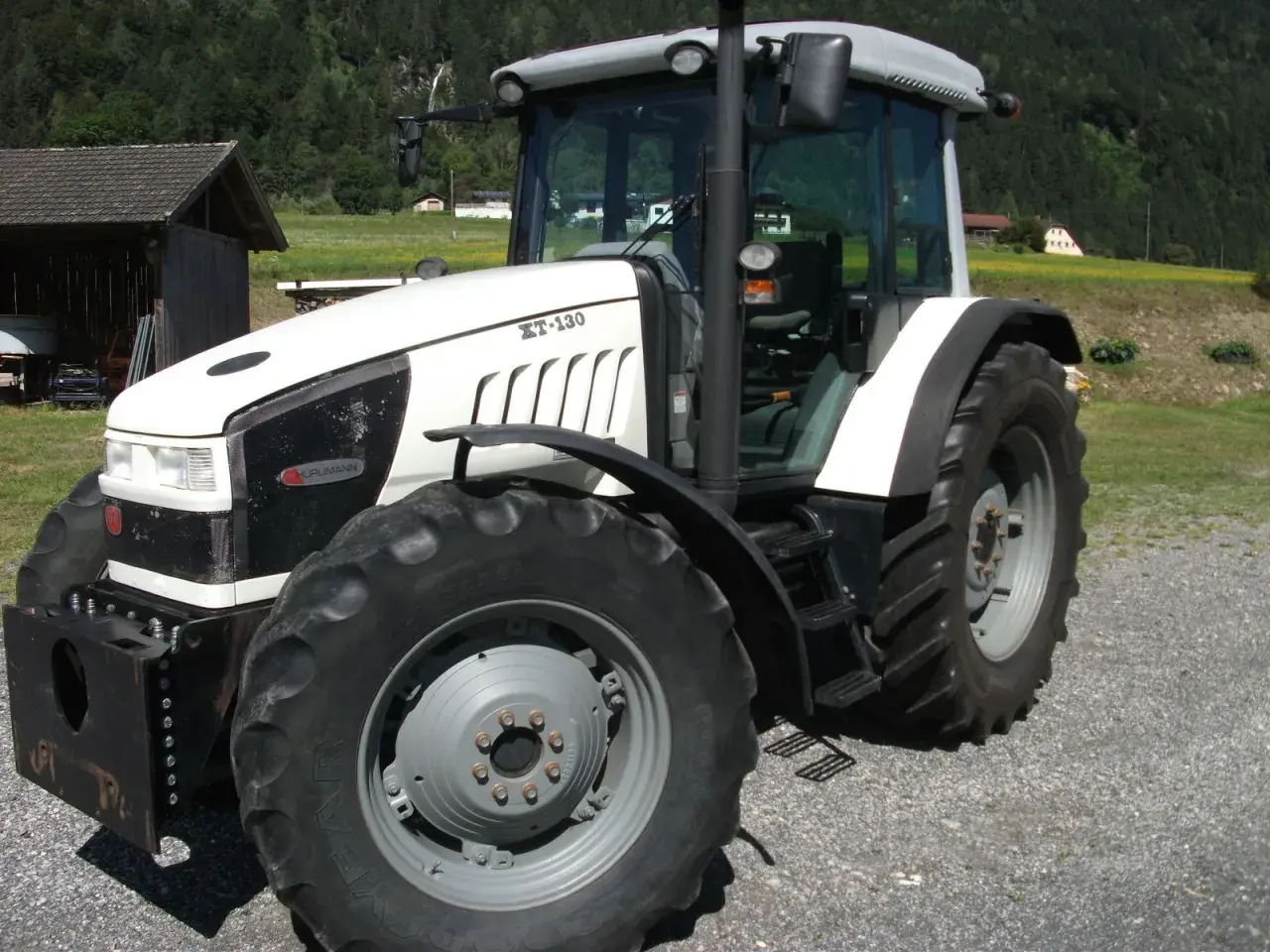 Biały traktor Hurlimann XT-130 na tle górskiego krajobrazu.
