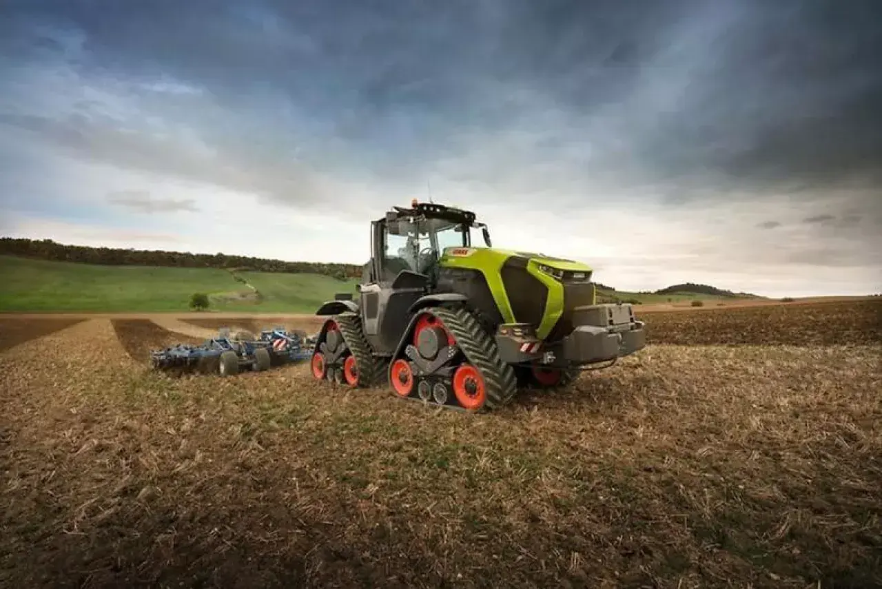 Potężny Claas Xerion z gąsienicami pracuje na polu, przygotowując ziemię do siewu.