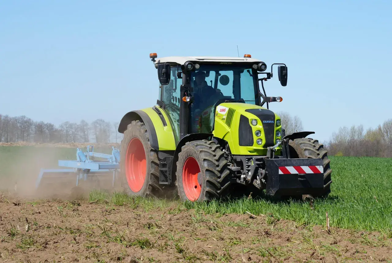 Zielony traktor Claas Arion 430 pracuje na polu, spulchniając ziemię.