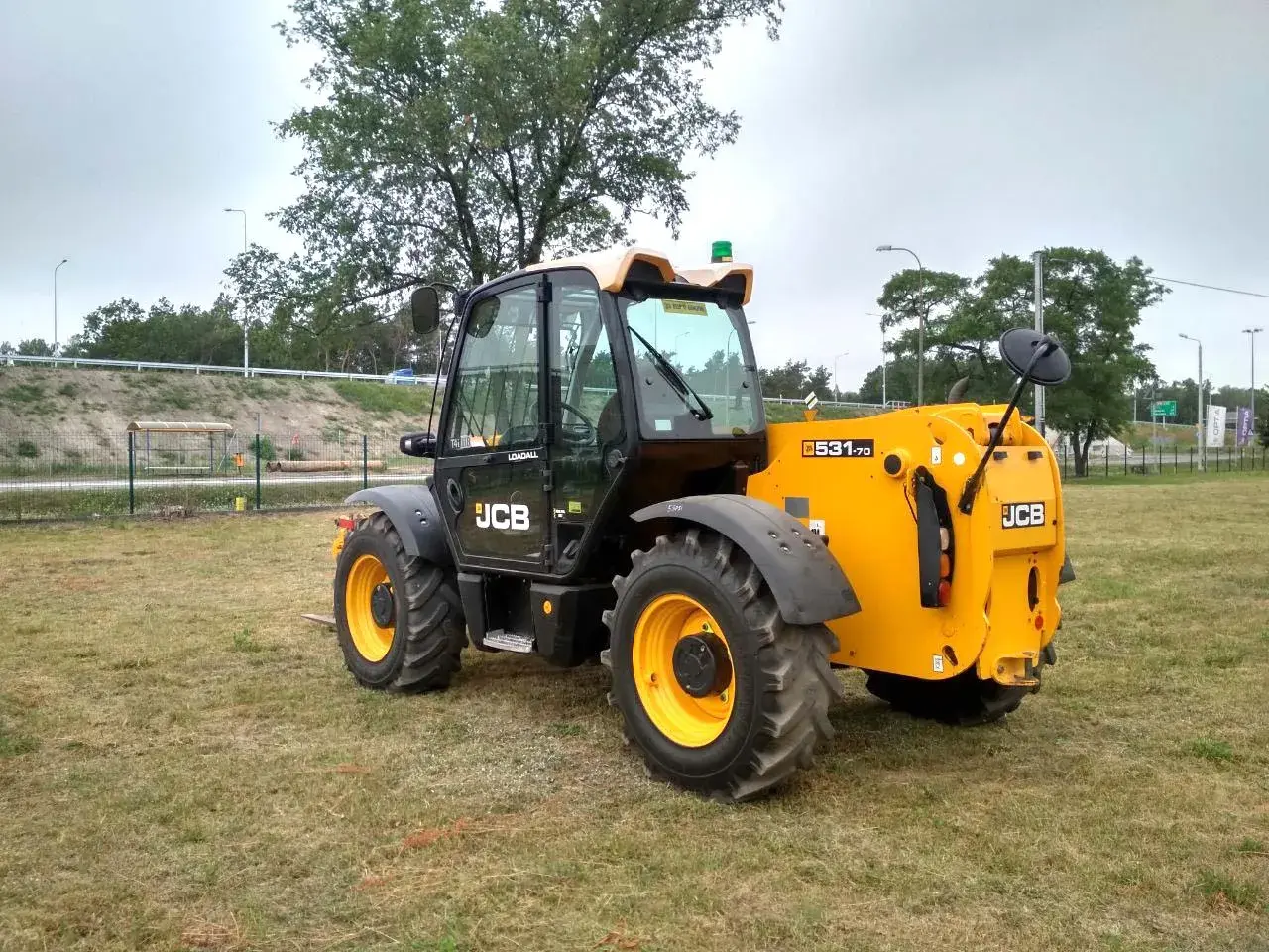 Żółty ładowarka teleskopowa JCB 531-70 stoi na trawiastym polu.