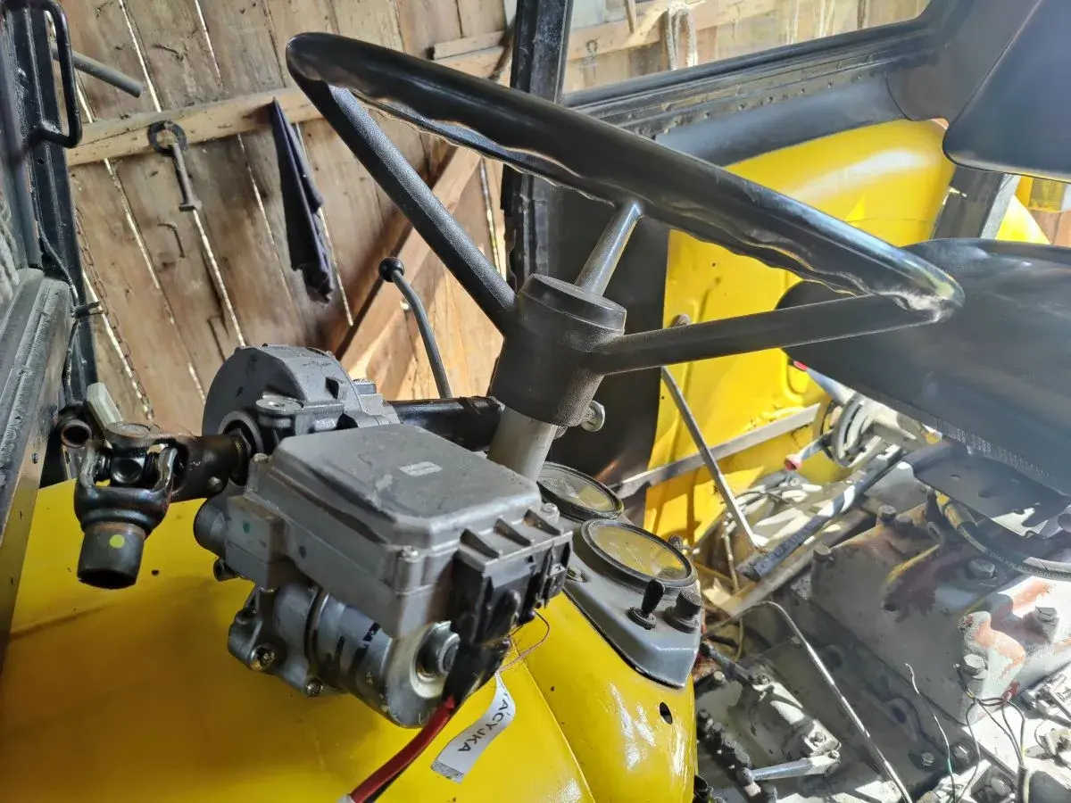 Mechanizm wspomagania kierownicy w żółtym ciągniku. Widoczna kolumna kierownicy, wał napędowy i elementy hydrauliczne.
