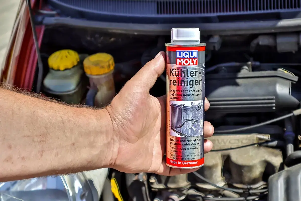 Dłoń trzyma puszkę płukanki do układu chłodzenia Liqui Moly, gotową do użycia w silniku samochodu.