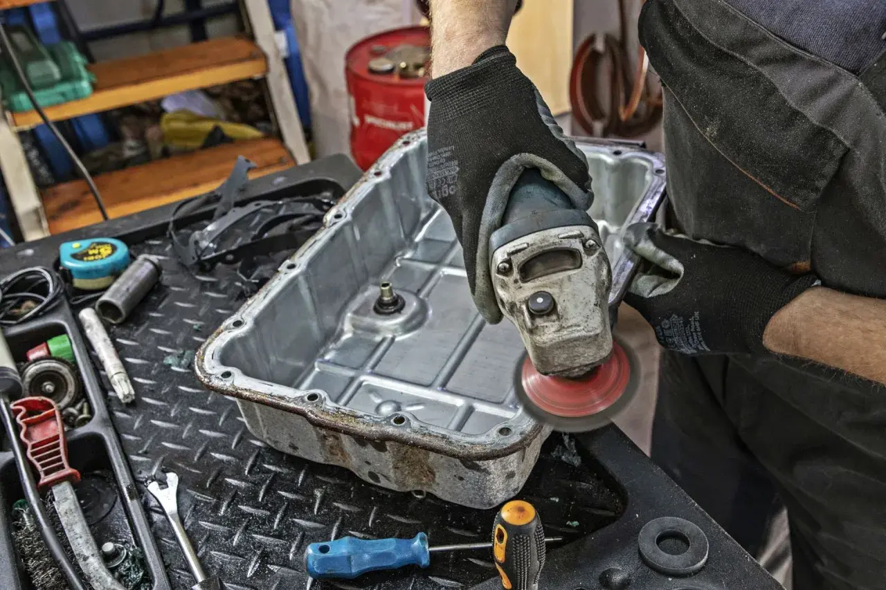 Mechanik szlifuje miskę olejową skrzyni biegów, przygotowując ją do wymiany oleju.