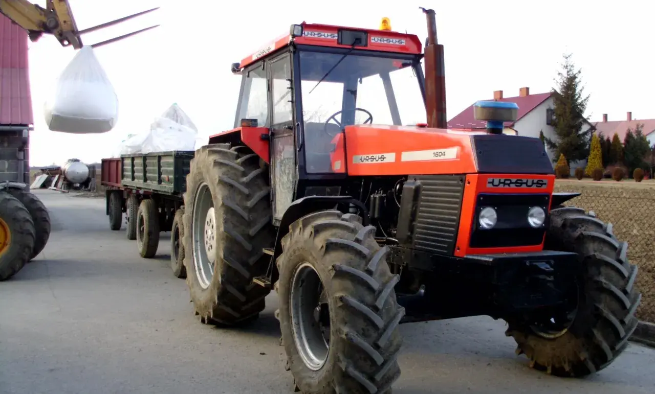 Czerwony Ursus 1604 z przyczepą załadowaną workami, gotowy do pracy na gospodarstwie.