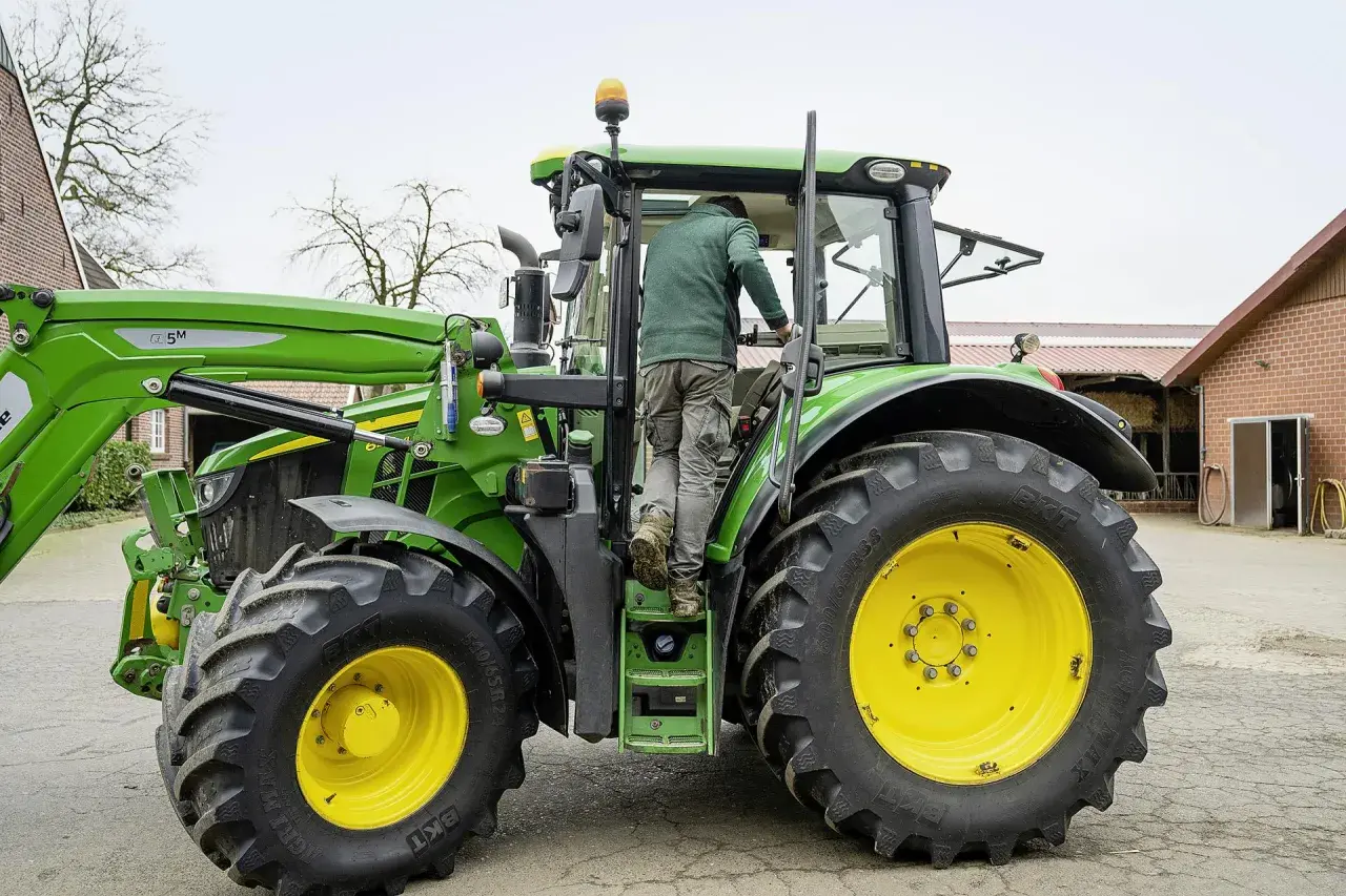 Rolnik wsiada do zielonego traktora John Deere, gotowy do pracy na gospodarstwie.