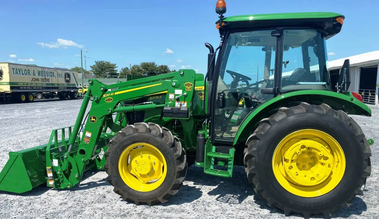 Zielony ciągnik John Deere 5075E z ładowaczem czołowym, gotowy do pracy na farmie.