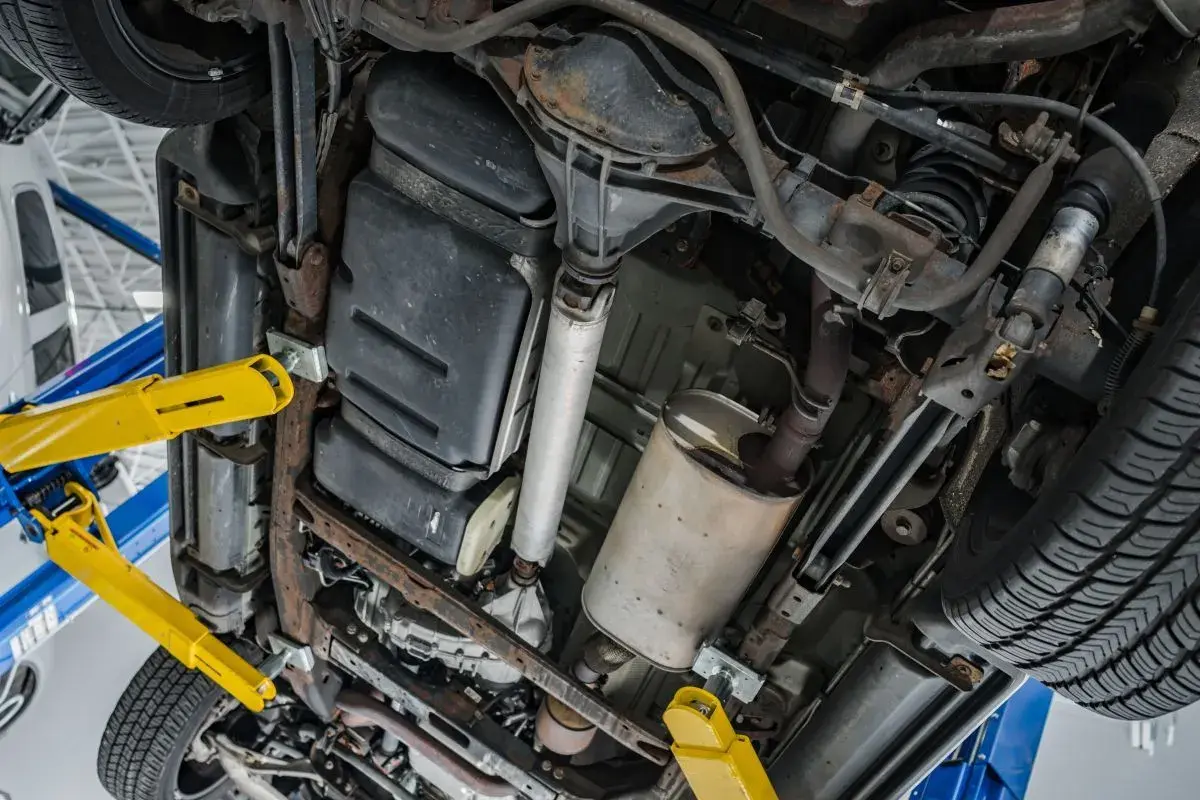 Podnośnik samochodowy podtrzymuje auto, ukazując podwozie z układem wydechowym i zbiornikiem paliwa. Czas na wypalanie DPF.