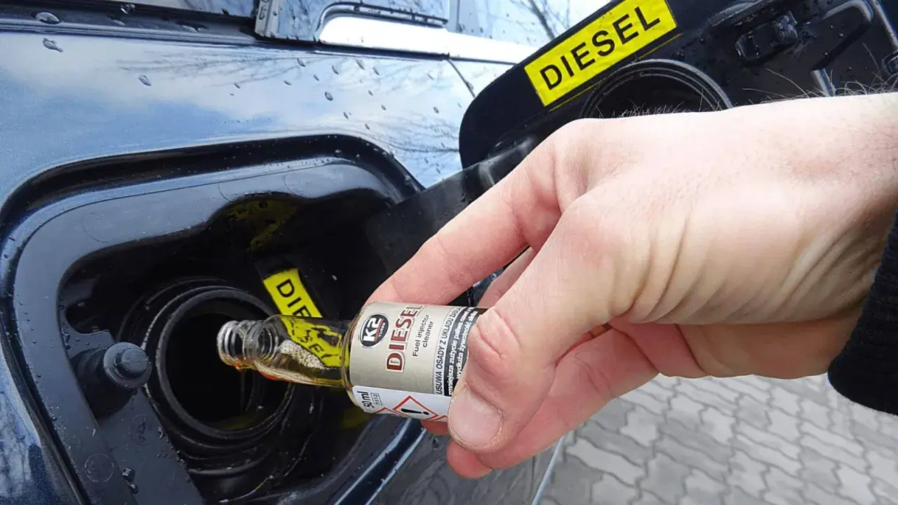 Dłoń wlewa dodatek do benzyny do baku samochodu z napisem DIESEL.