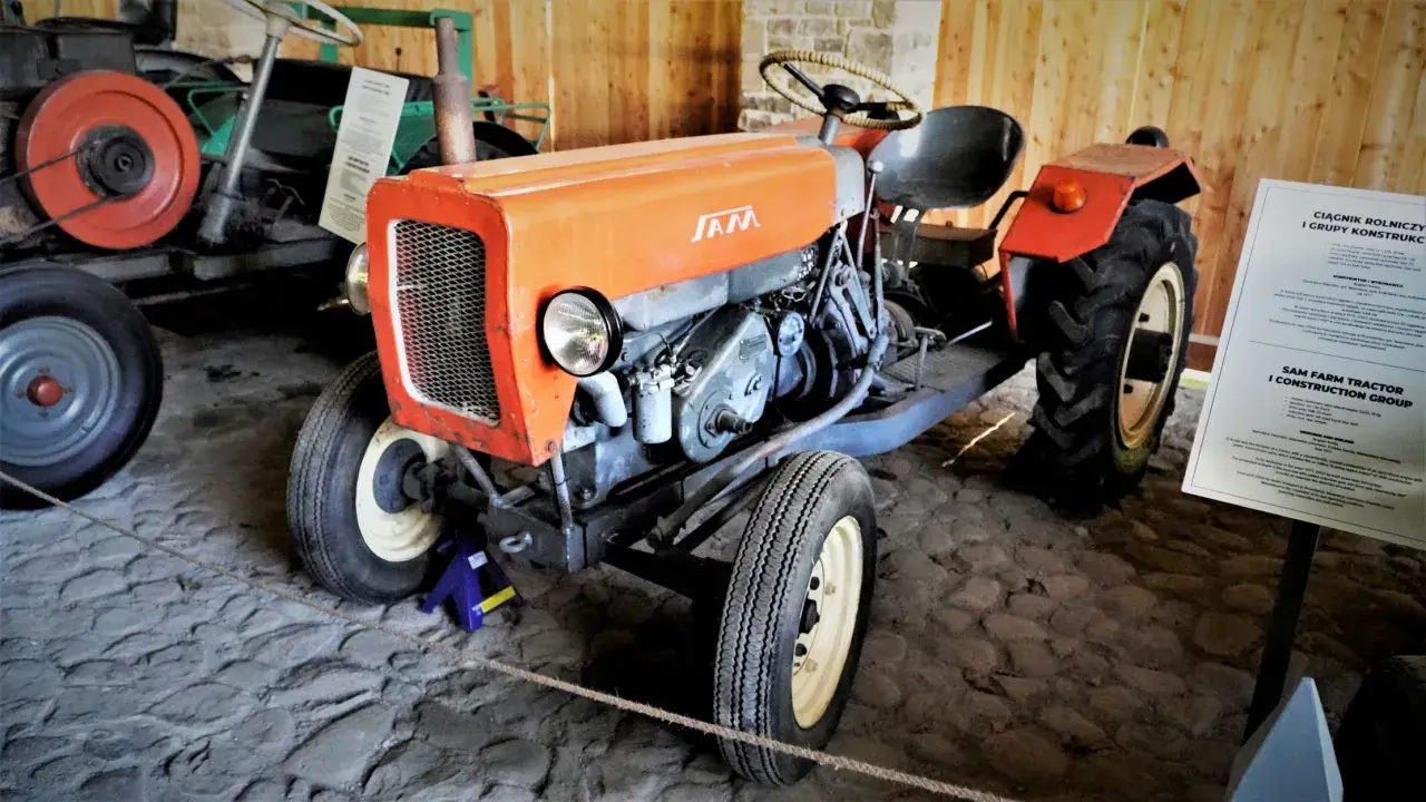 Pomarańczowy traktor SAM, znany jako esiok, z charakterystycznym grillem i silnikiem.