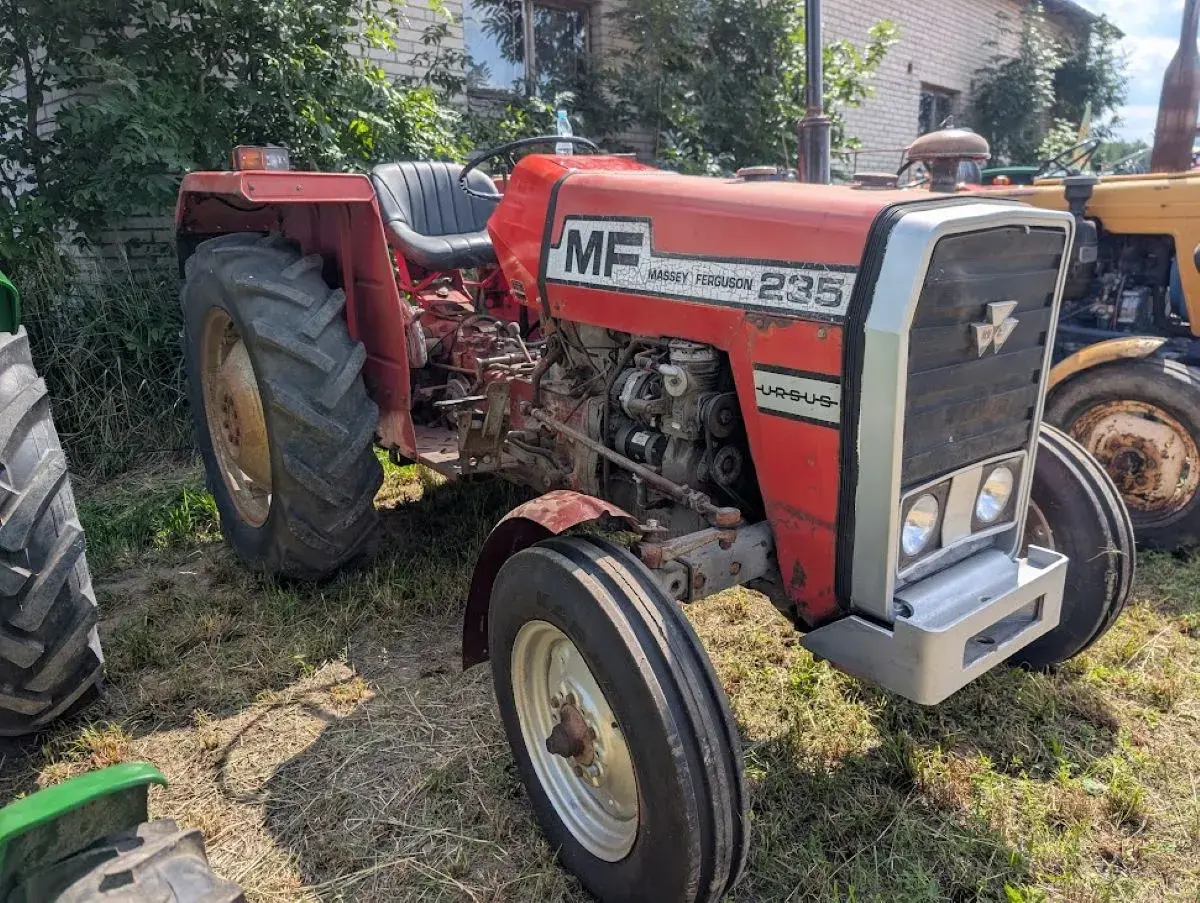 Czerwony Massey Ferguson 235 z napisem "Ursus" na masce, gotowy do pracy na polu.