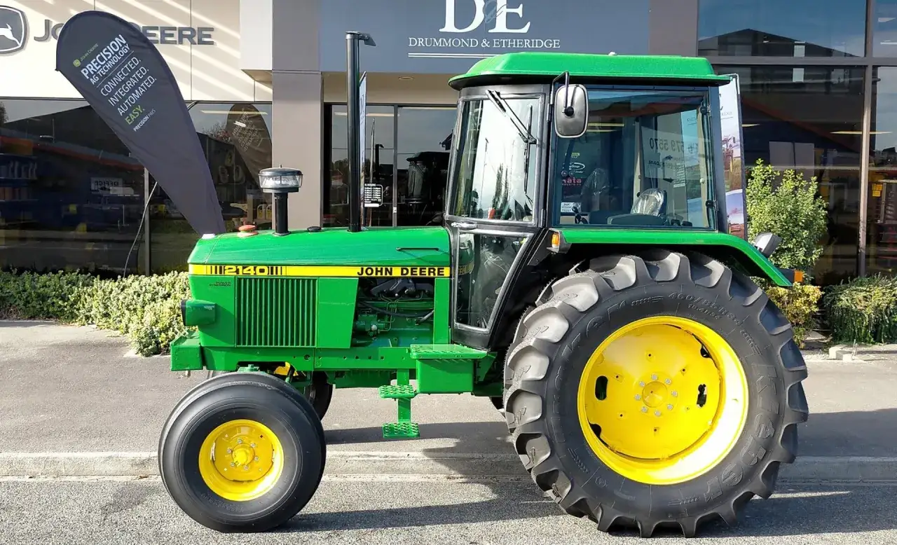 Zielony traktor John Deere 2140 z żółtymi felgami stoi przed budynkiem dealera.