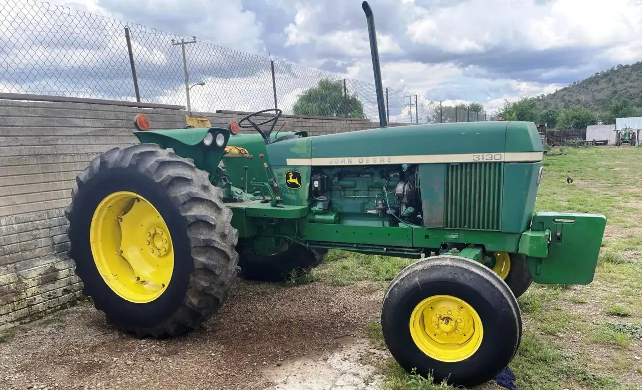 Zielony John Deere 3130 z żółtymi felgami stoi na żwirowym podwórku, gotowy do pracy.