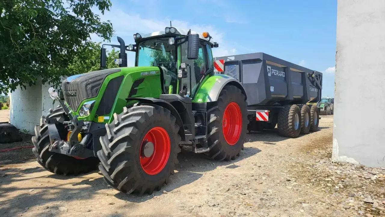 Zielony traktor Fendt 828 z przyczepą Perard gotowy do pracy na polnej drodze.
