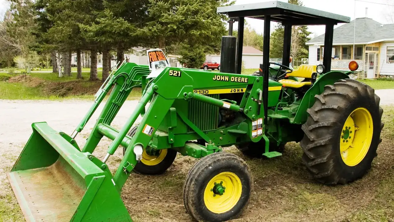 Zielony traktor John Deere 2130 z ładowaczem czołowym stoi na podwórku.