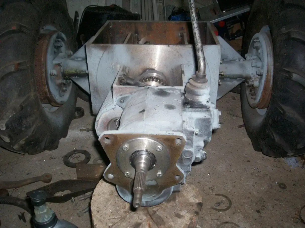 Elementy mechaniczne do budowy ciągnika sam. Widoczne koła, skrzynia biegów i wał napędowy.