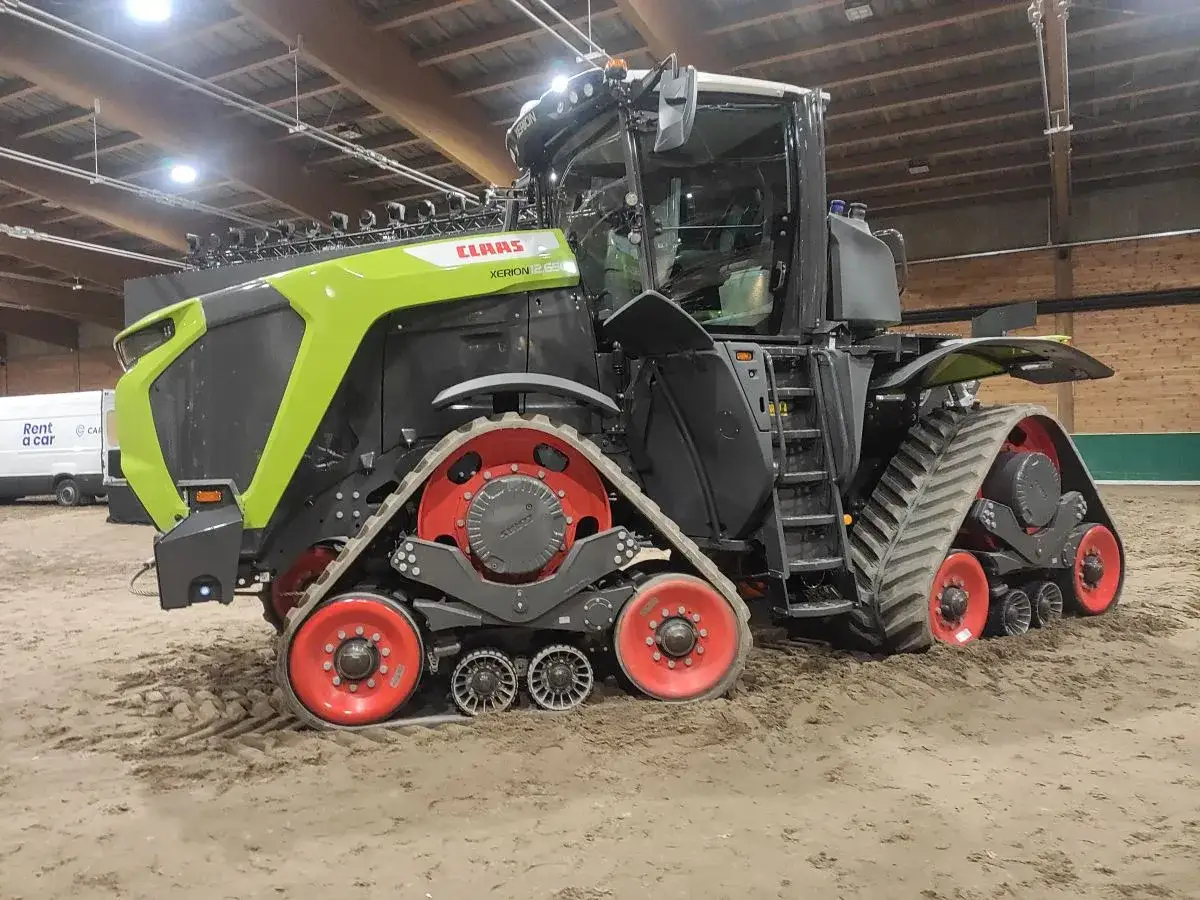 Potężny Claas Xerion na gąsienicach, gotowy do pracy na polu. Czerwone felgi dodają mu charakteru.