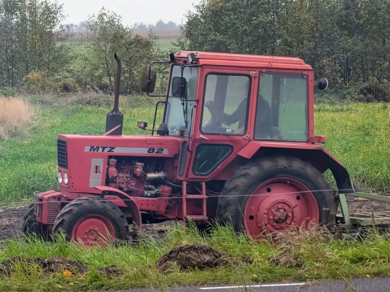 Czerwony traktor MTZ Belarus 820 pracuje na polu, za nim widać las.