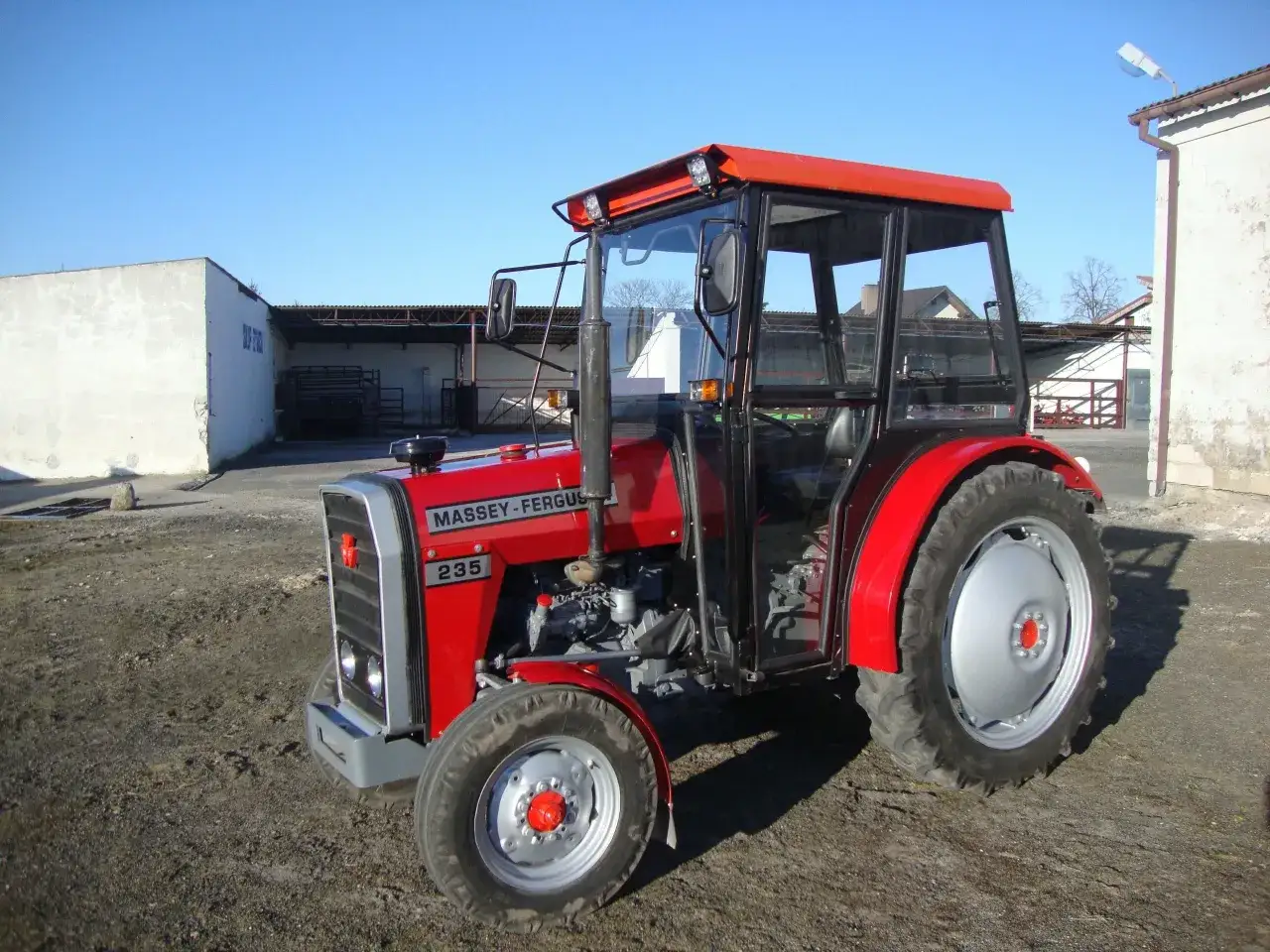 Czerwony traktor Massey Ferguson 235 z kabiną stoi na podwórzu.