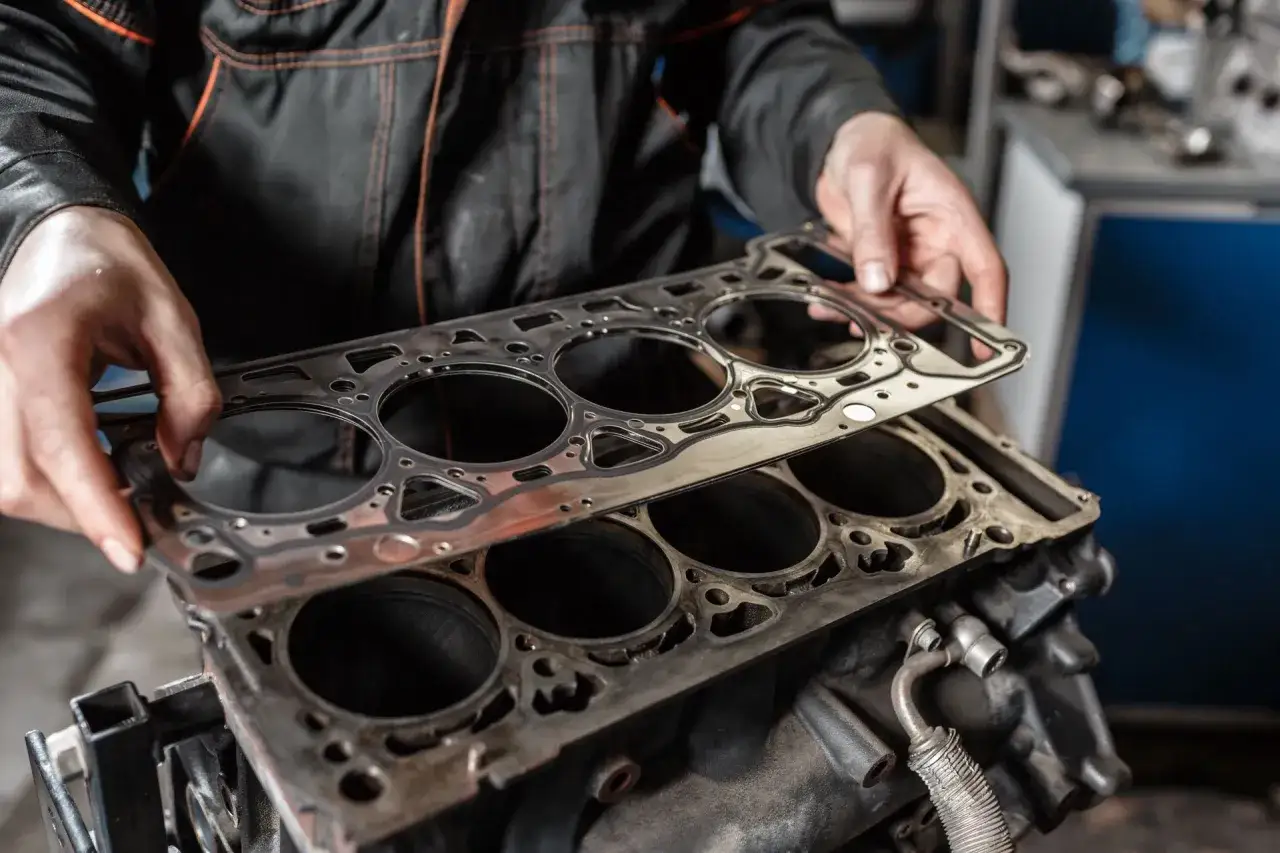 Mechanik trzyma nową uszczelkę pod głowicę, przygotowując się do jej wymiany. Sprawdź wymiana uszczelki pod głowicą cennik.