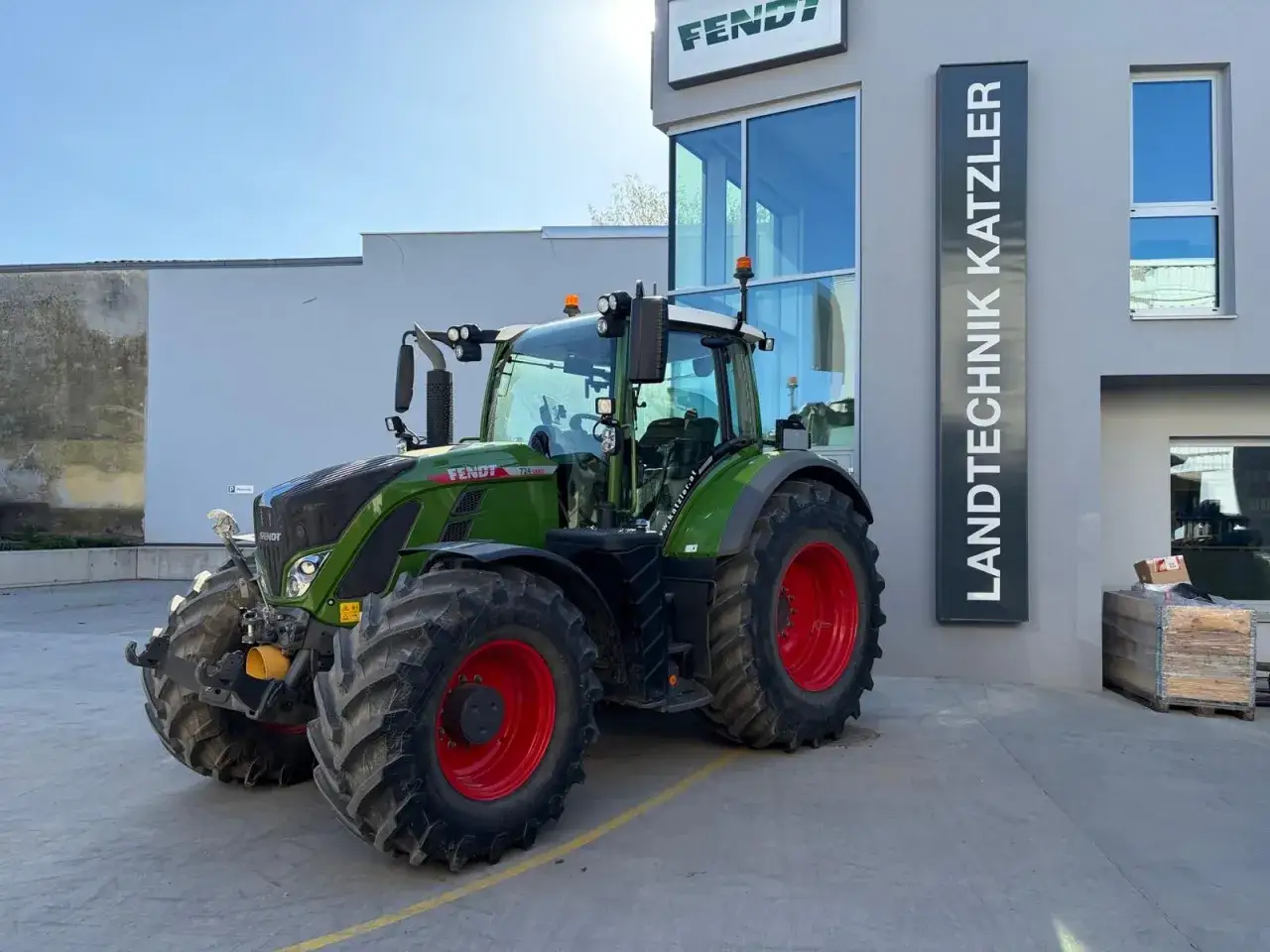 Zielony traktor Fendt 724 Vario z czerwonymi felgami stoi przed budynkiem Landtechnik Katzler.