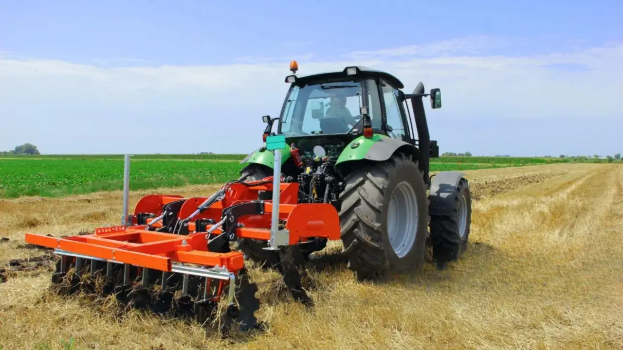 Zielony traktor wykonuje podorywkę na polu, przygotowując ziemię do kolejnych prac.