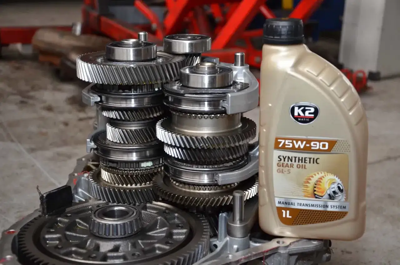 Gotowe do wymiany oleju w skrzyni biegów. Widoczne elementy przekładni i butelka oleju syntetycznego 75W-90.