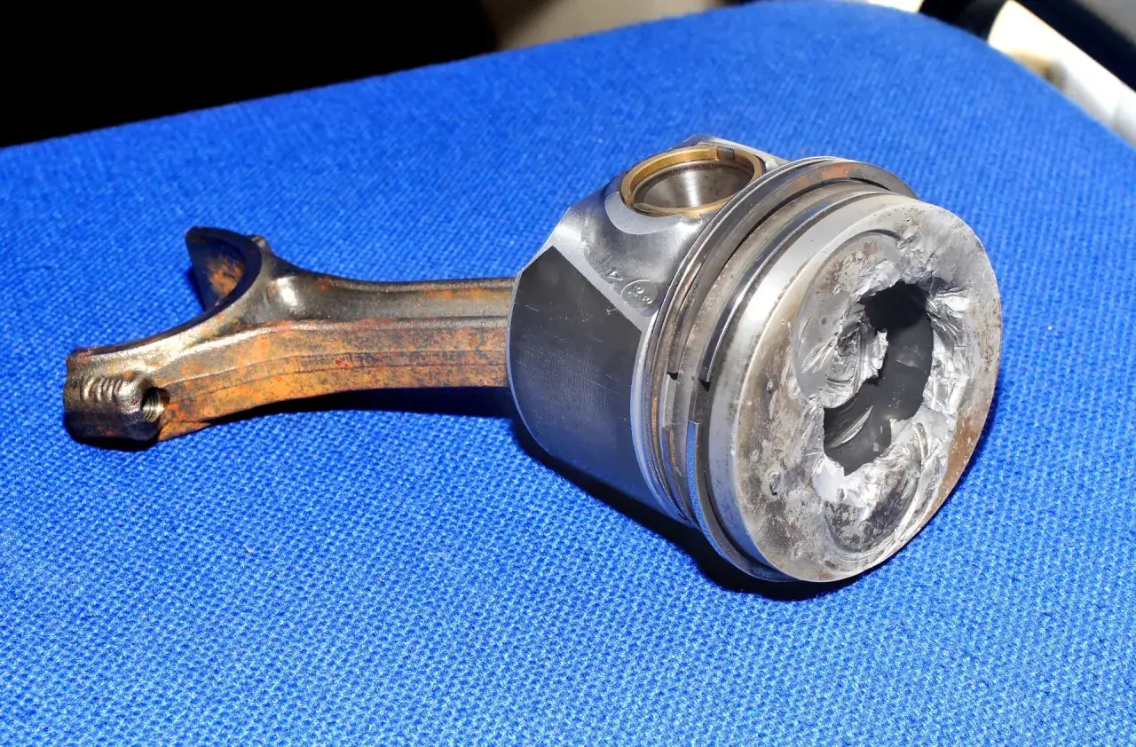 Uszkodzony tłok z korbowodem, element bloku silnika, nosi ślady poważnych uszkodzeń mechanicznych.