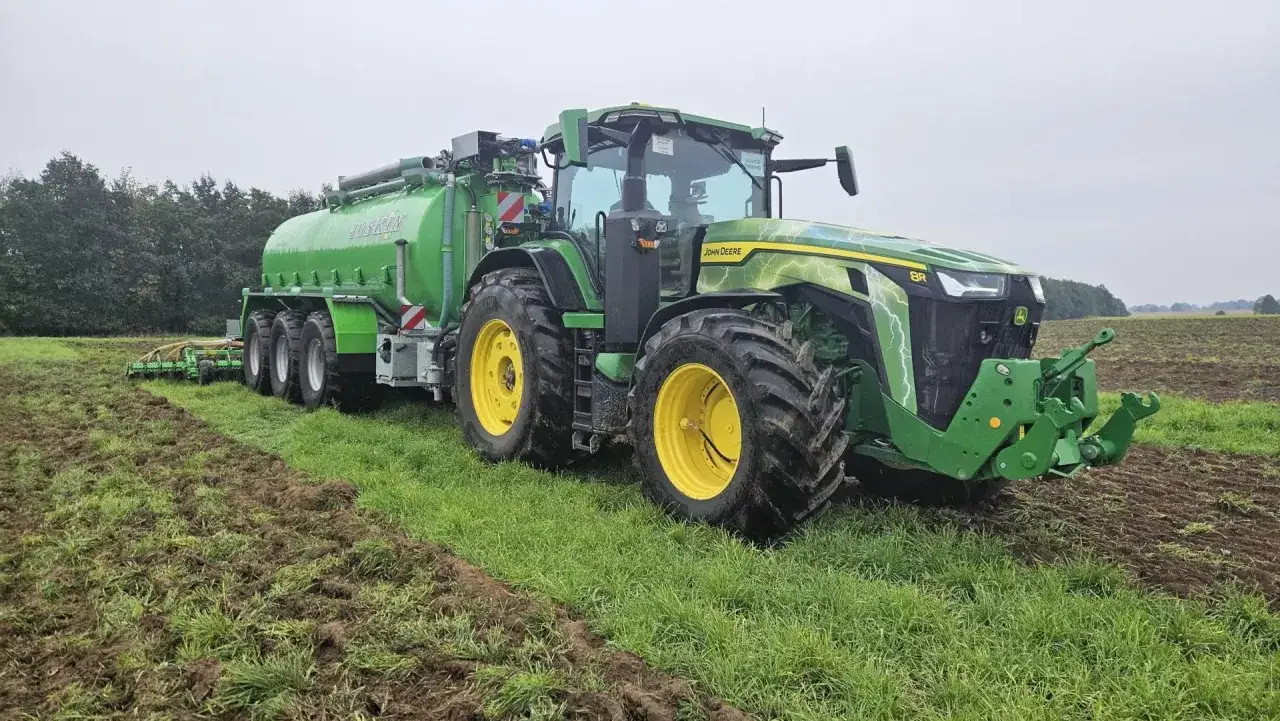 Potężny John Deere z przyczepą asenizacyjną pracuje na polu, przygotowując ziemię do siewu.