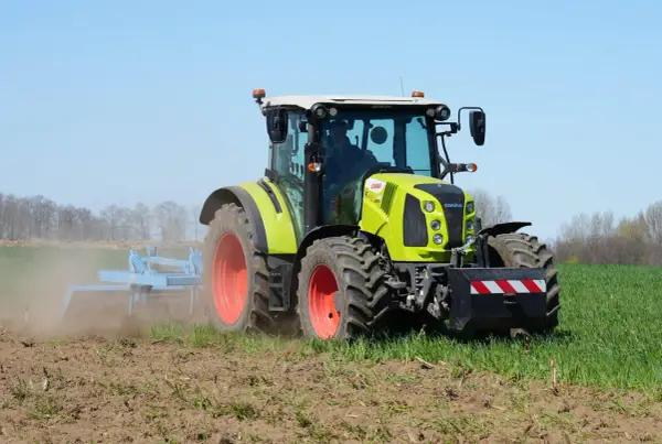Zielony traktor Claas Arion 430 pracuje na polu, spulchniając ziemię.